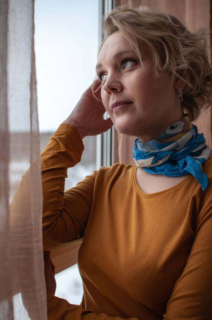 Portrait of a happy blonde woman at home by the window in the afternoon - Photo, Image
