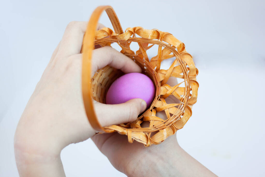 A mão alcança um ovo pintado para o feriado de Páscoa o ovo está em uma pequena cesta foco seletivo
 - Foto, Imagem
