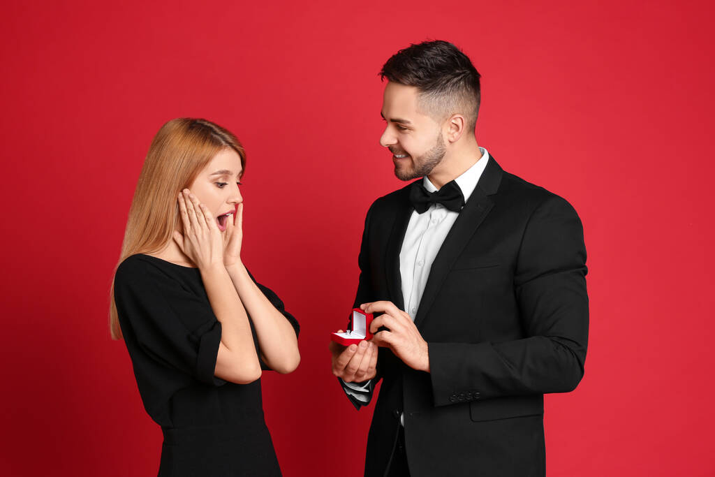Uomo con anello di fidanzamento fare proposta di matrimonio alla fidanzata su sfondo rosso
 - Foto, immagini