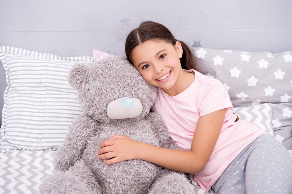 Pure love concept. Kids evening routines. Favorite toy. Girl child hug teddy bear in her bedroom. Pleasant time in cozy bedroom. Girl kid long hair cute pajamas relax and play plush teddy bear toy - Photo, Image