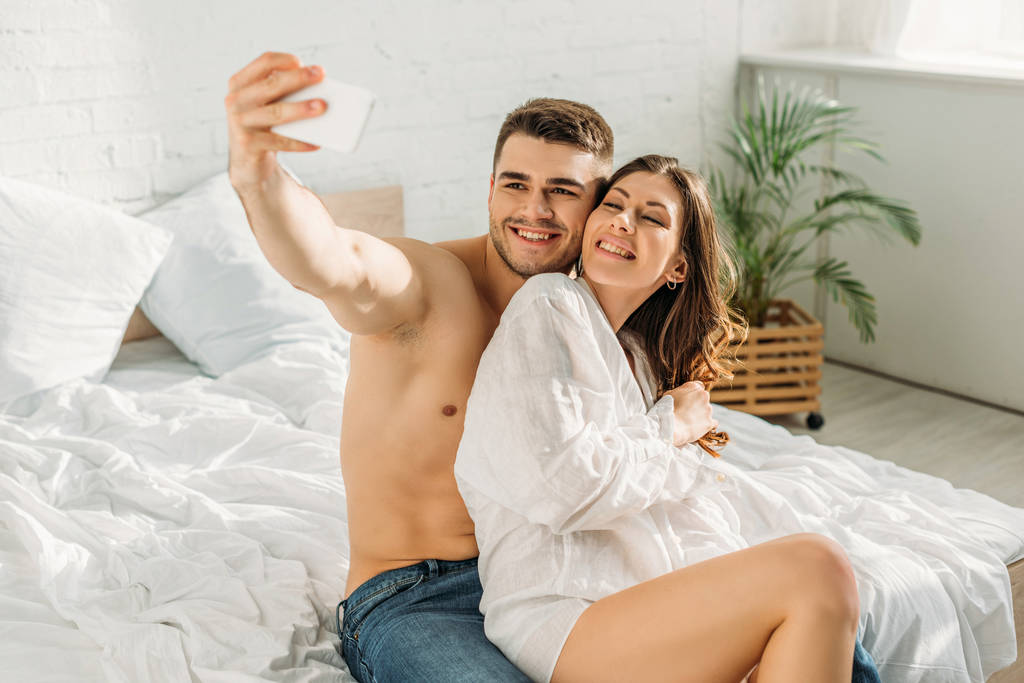 boldog félmeztelen férfi csinál szelfi okostelefon boldog barátnő fehér ingben - Fotó, kép