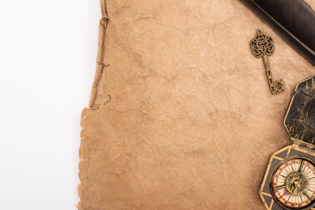 bovenaanzicht van veer, vintage sleutel en kompas op oud papier geïsoleerd op wit - Foto, afbeelding