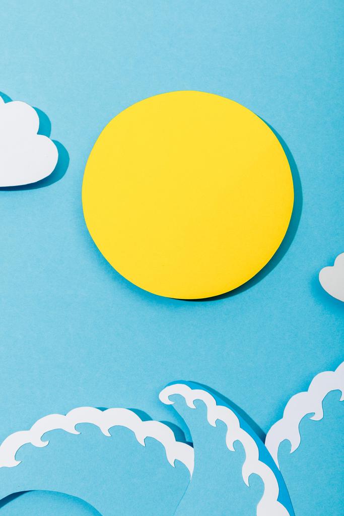 Top näkymä paperi leikkaa aurinko, pilvet ja meri-aallot sinisellä pohjalla
 - Valokuva, kuva