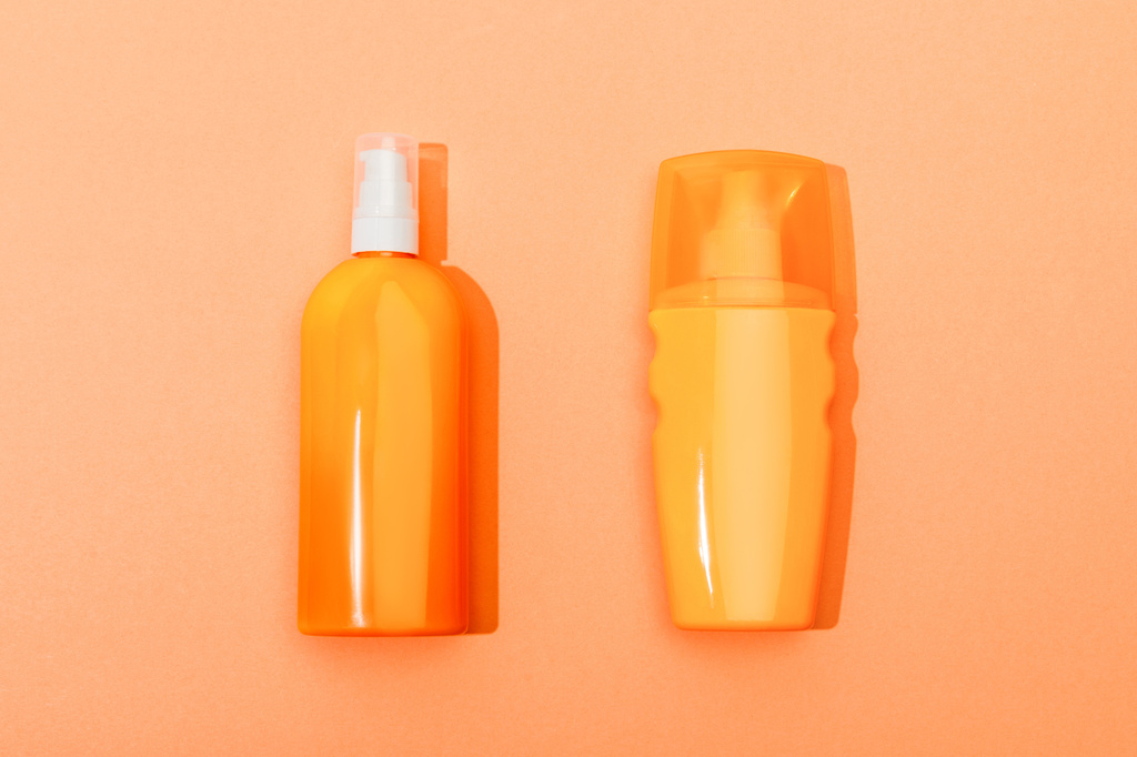 Вид сверху на бутылку солнцезащитного крема на оранжевом фоне
 - Фото, изображение