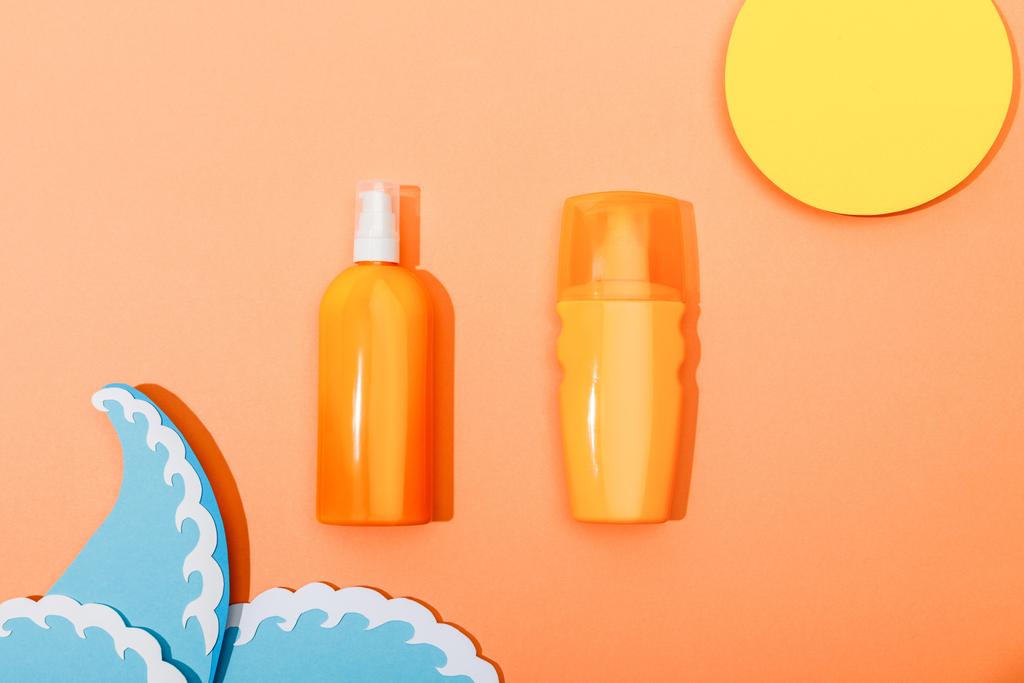 Vista superior de botellas dispensadoras de protector solar con sol cortado en papel y ondas marinas sobre fondo naranja
 - Foto, Imagen
