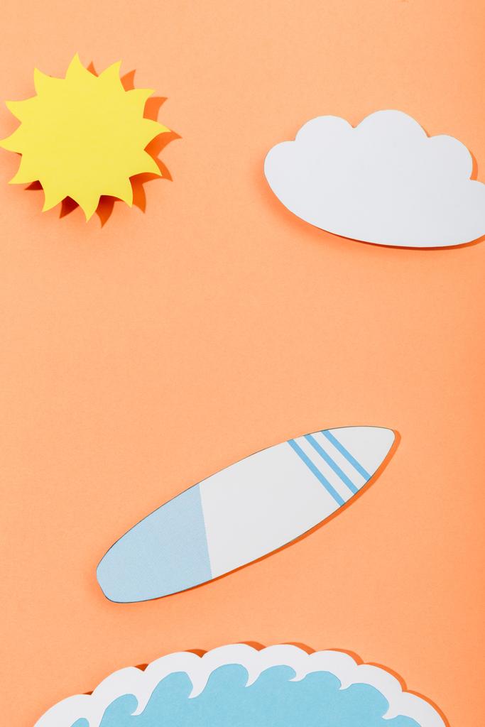 Top näkymä paperi leikata aurinko, pilvi, surffilauta ja meri aalto oranssi tausta
 - Valokuva, kuva
