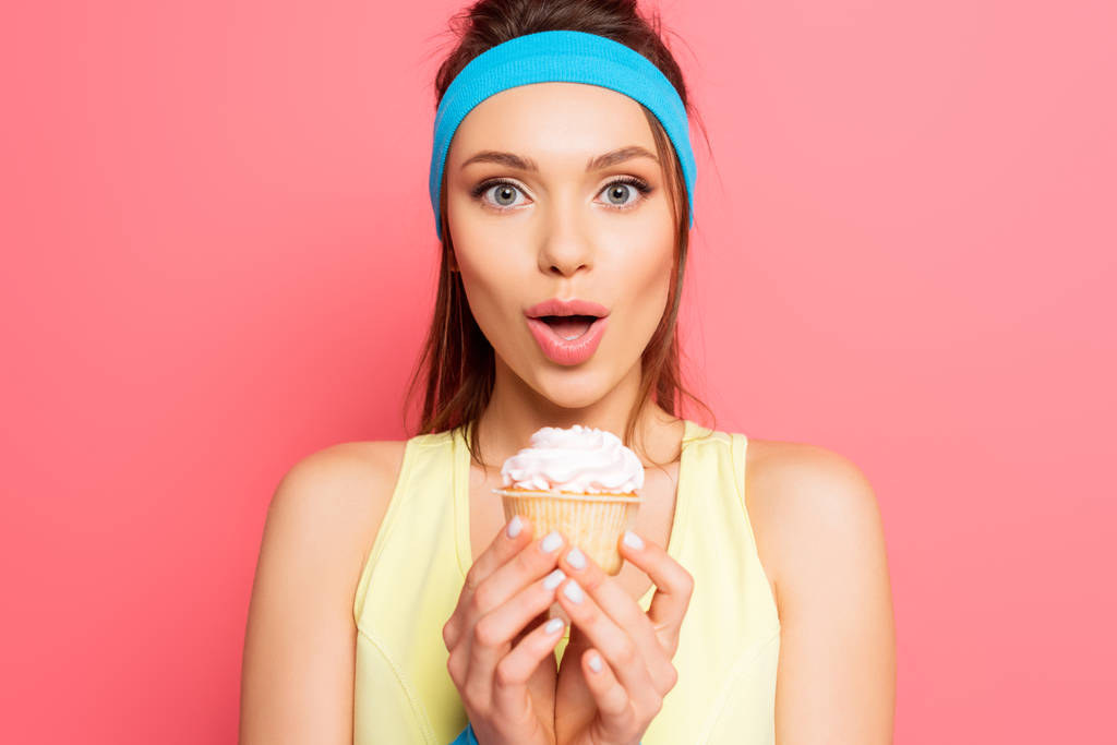 izgatott sportnő kezében finom cupcake miközben nézi a kamera rózsaszín háttér - Fotó, kép