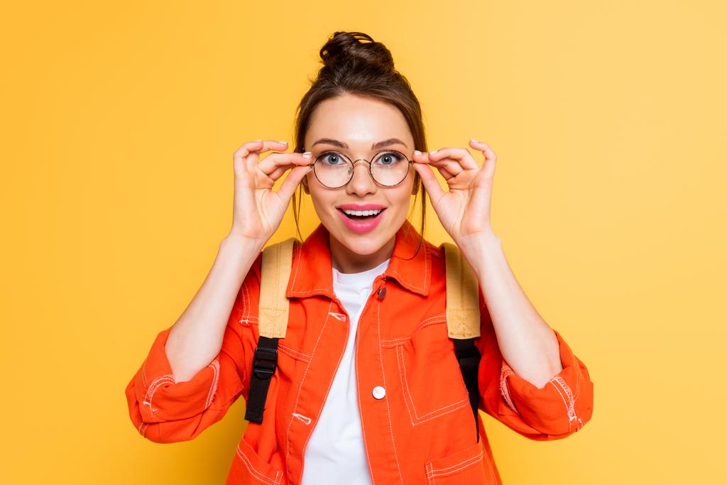 surprised student touching glasses while looking at camera on yellow background - Photo, Image