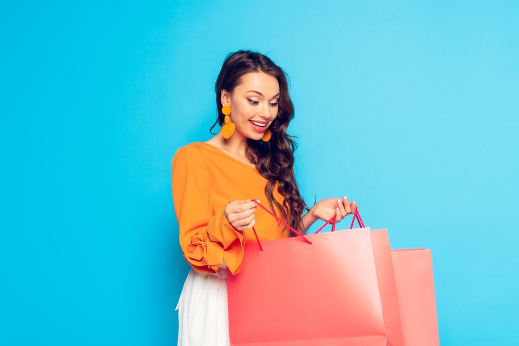 привлекательная возбужденная девушка смотрит в сумку для покупок на голубом фоне
 - Фото, изображение