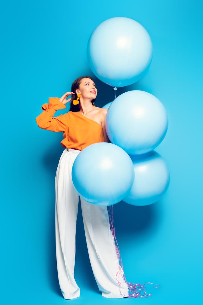 full length άποψη του ευτυχισμένη μοντέρνα γυναίκα με μεγάλα εορταστικά μπαλόνια σε μπλε φόντο - Φωτογραφία, εικόνα