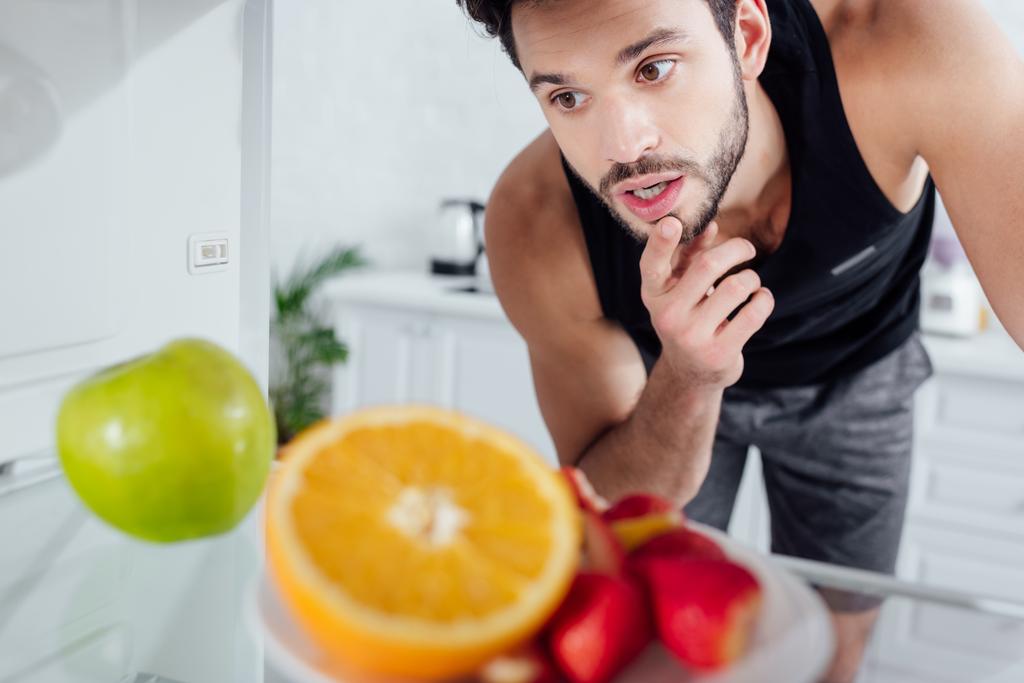 selektivní zaměření zamyšleného muže při pohledu na ovoce v ledničce  - Fotografie, Obrázek
