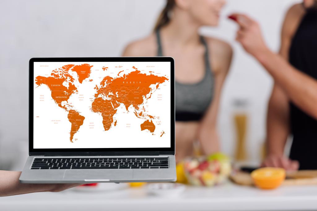 selective focus of laptop with world map on screen near couple in kitchen  - Photo, Image