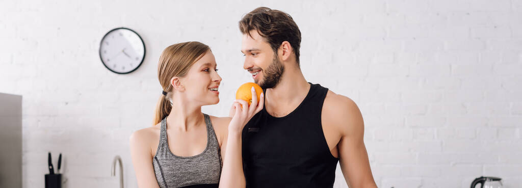 panoramic shot of happy girl holding orange and looking at cheerful man  - Photo, Image