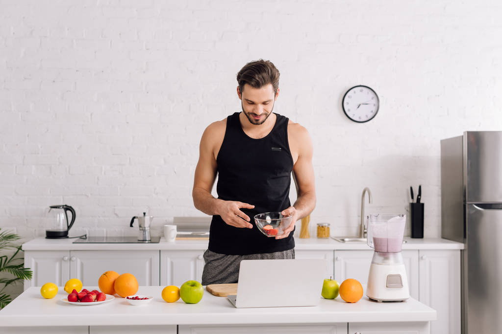 bel homme regardant ordinateur portable près de fruits savoureux et mélangeur avec smoothie
  - Photo, image