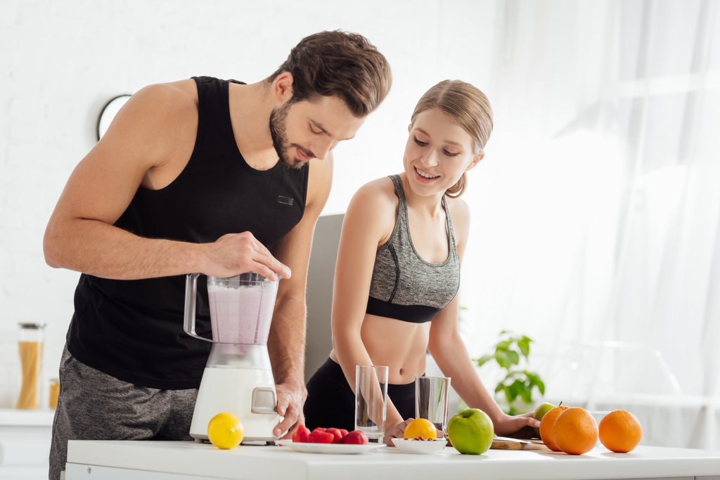 спортивный человек готовит смузи рядом счастливая девушка и фрукты
  - Фото, изображение