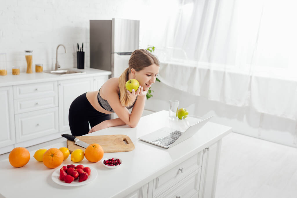 щаслива і спортивна жінка зі смачним яблуком дивиться на ноутбук
  - Фото, зображення