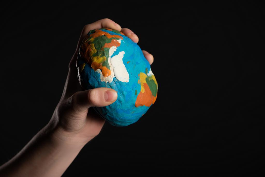 Vue recadrée du globe de plasticine dans une main féminine isolée sur un concept noir de réchauffement climatique
 - Photo, image