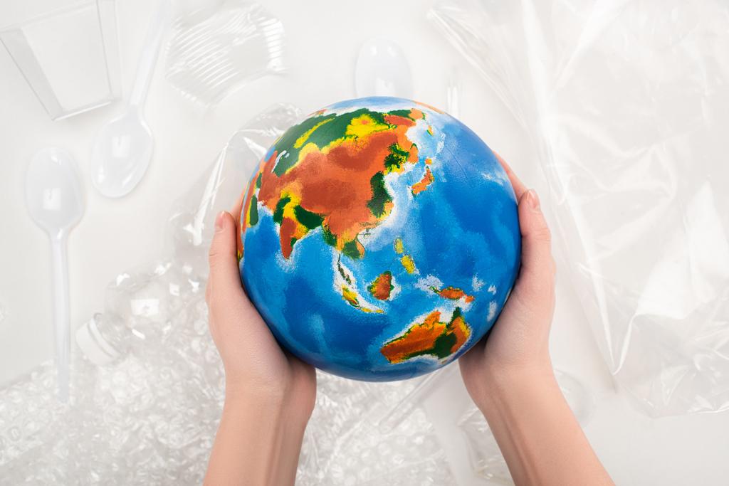 Widok kobiety trzymającej kulę ziemską nad plastikowymi śmieciami na białym tle, koncepcja globalnego ocieplenia - Zdjęcie, obraz