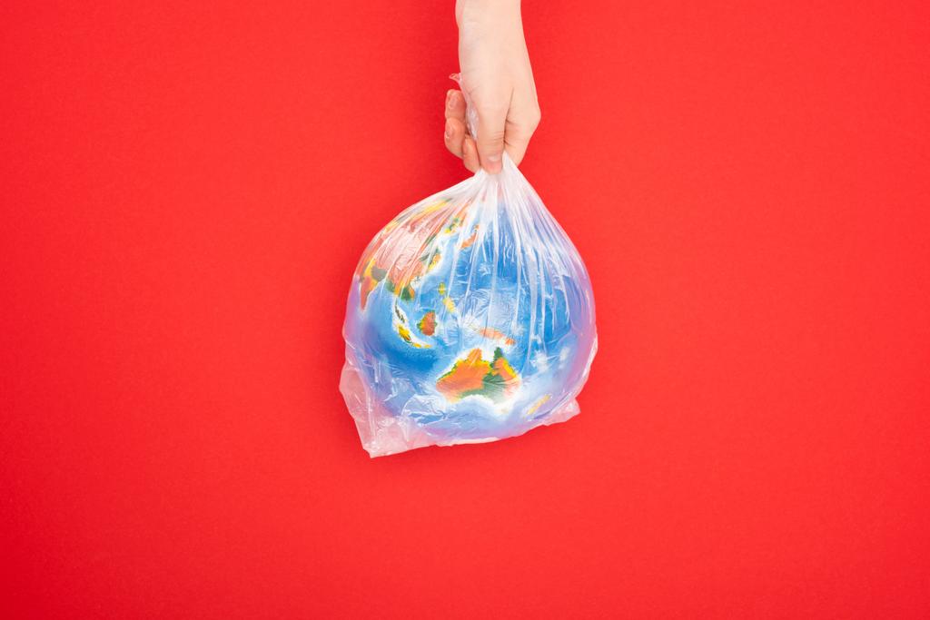 Ausgeschnittene Ansicht der Frau mit Globus in Plastiktüte isoliert auf rotem Hintergrund, Konzept der globalen Erwärmung - Foto, Bild