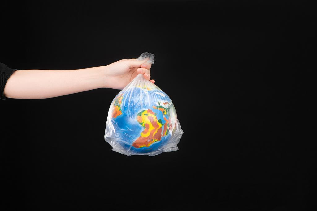 Cropped view of woman holding plastic bag with globe isolated on black, global warming concept - Photo, Image