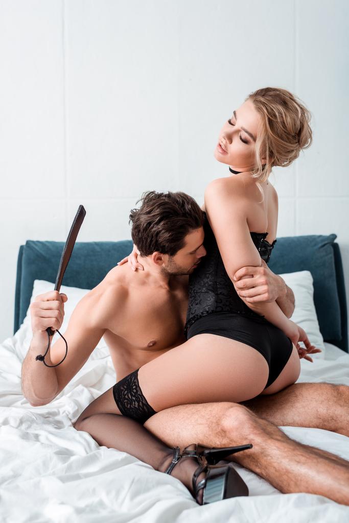 dominantní muž drží výprask pádlo v blízkosti submisivní žena  - Fotografie, Obrázek