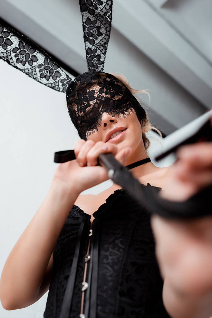 vista de ángulo bajo de la mujer con los ojos vendados en la máscara de conejo celebración látigo flagelación
  - Foto, Imagen