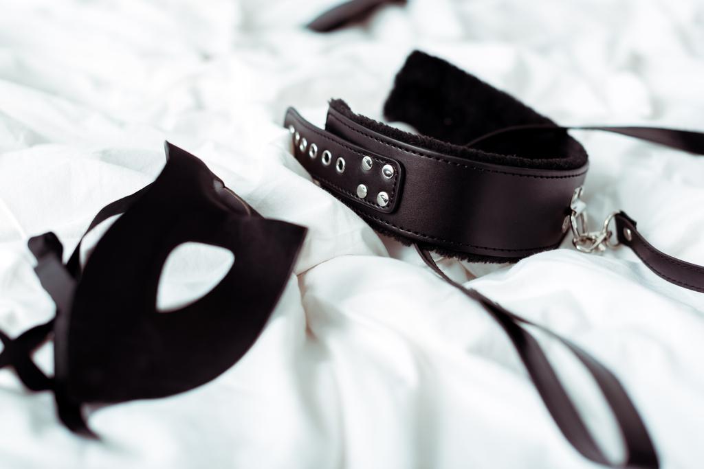 selectieve focus van bdsm riem en oogmasker op wit beddengoed  - Foto, afbeelding