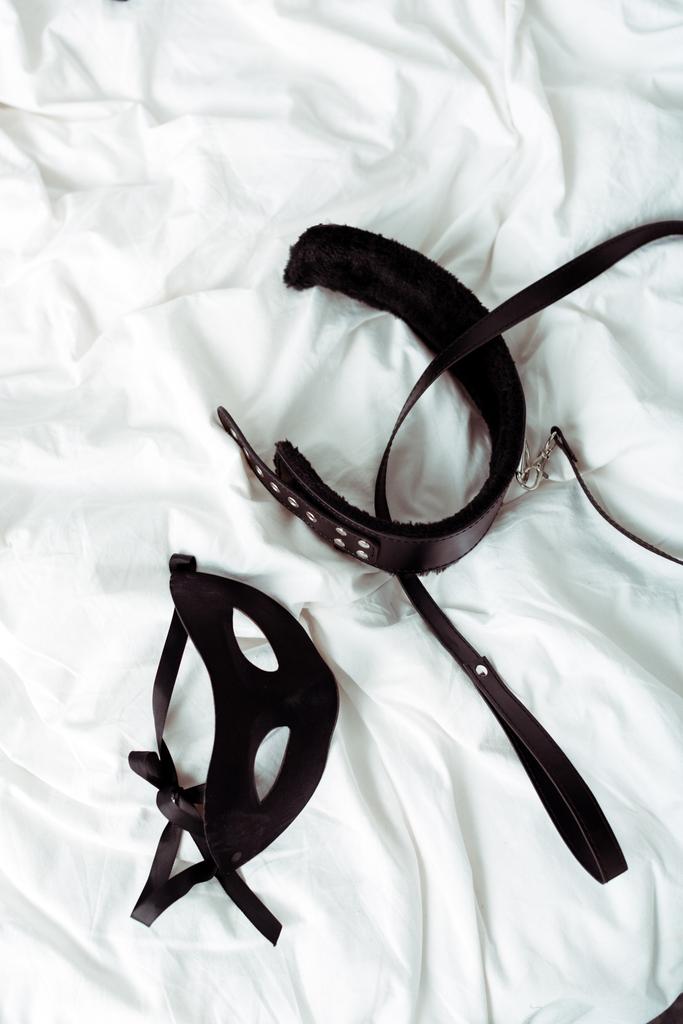 bovenaanzicht van bdsm riem en oogmasker op wit beddengoed  - Foto, afbeelding