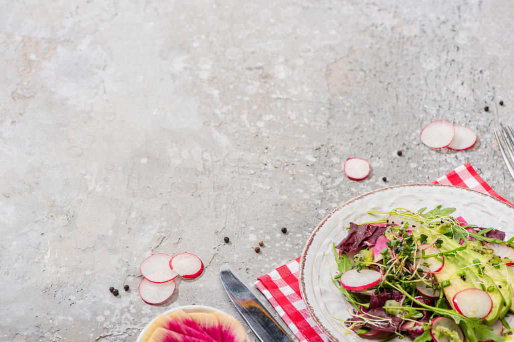 fresh radish salad with greens and avocado served on napkin with cutlery on grey concrete surface - Photo, Image