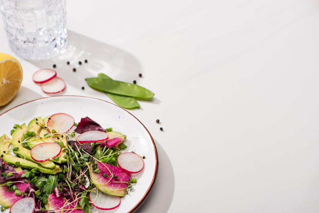 свежий салат из редьки с зеленью и авокадо на тарелке на белой поверхности с водой
 - Фото, изображение