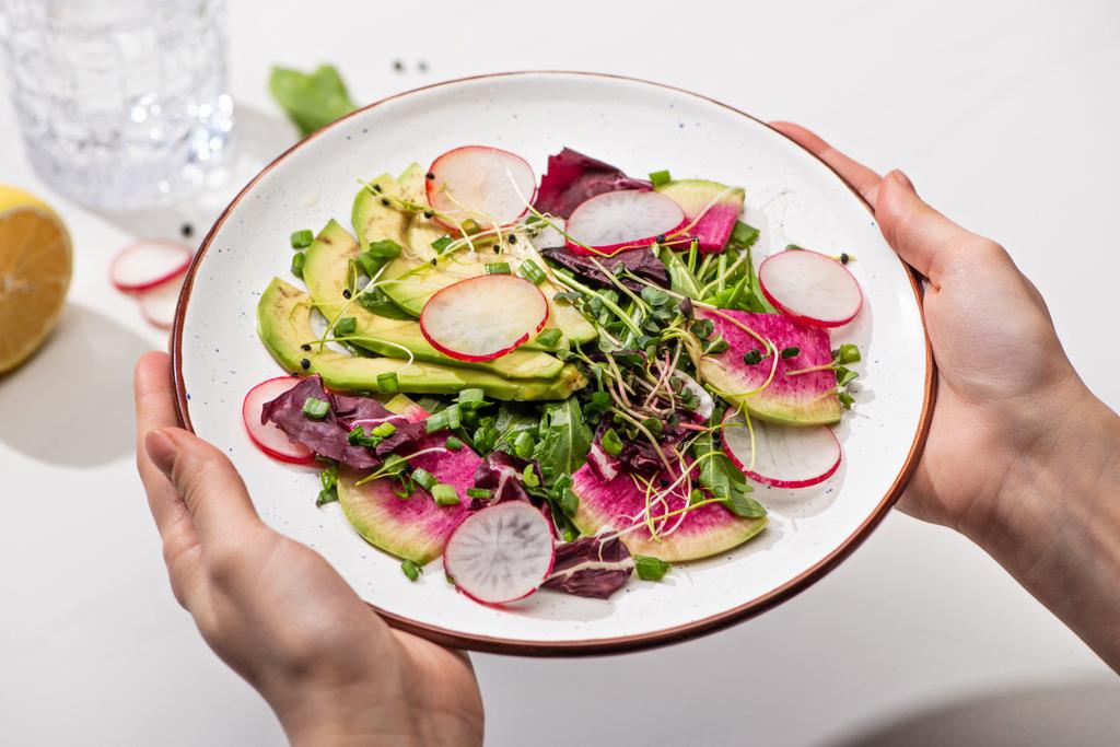 vágott kilátás nő gazdaság friss retek saláta zöldekkel és avokádó tányéron - Fotó, kép