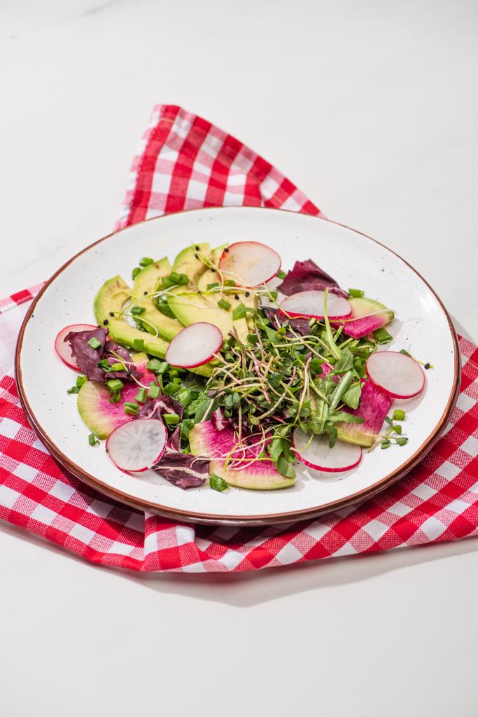 Frischer Rettichsalat mit Gemüse und Avocado auf Teller auf weißer Oberfläche mit Serviette - Foto, Bild