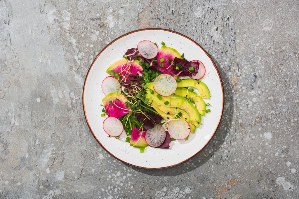top view of fresh radish salad with greens and avocado on grey concrete surface - Photo, Image