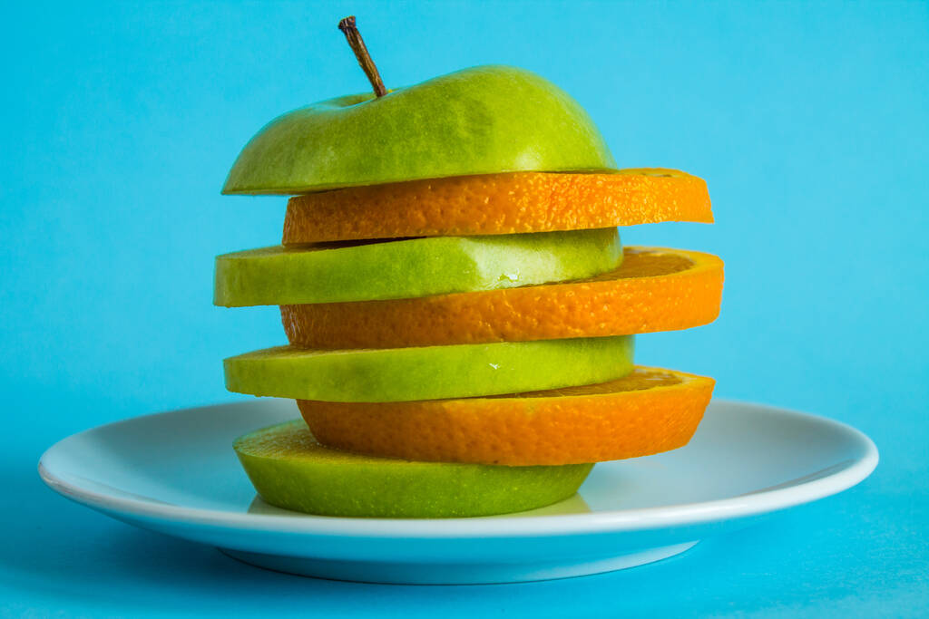 Alternatif elma ve portakal dilimlerini beyaz bir tabakta parlak mavi arka planda yakın plan çekimde. Kavram - sağlıklı yiyecek, vitamin, meyve, karışım - Fotoğraf, Görsel