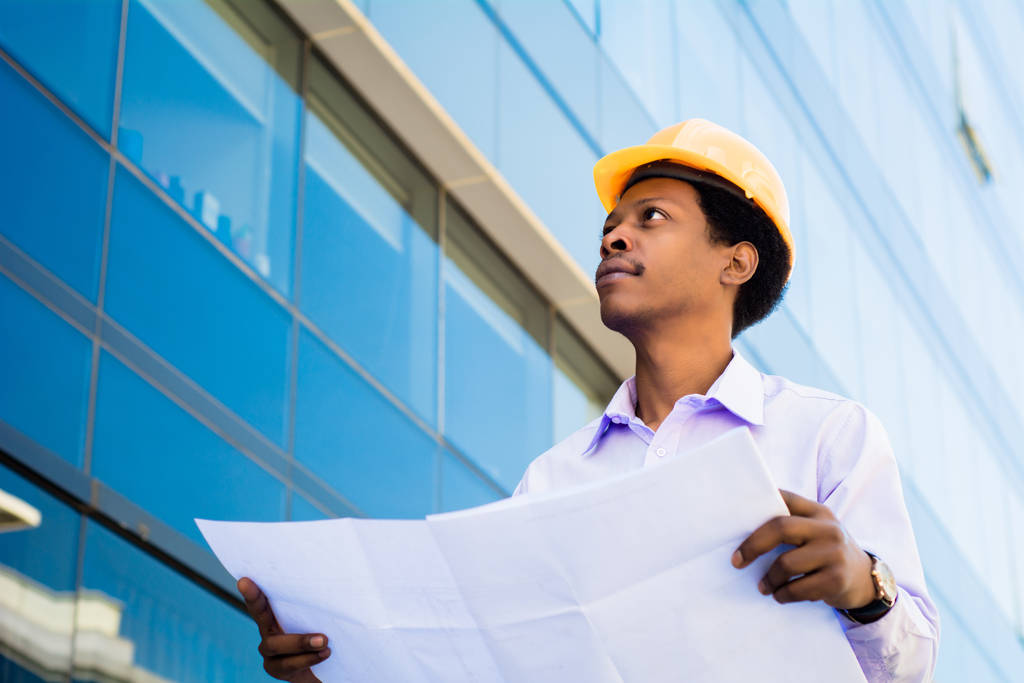 Portrét profesionálního architekta v helmě při pohledu na modré tisky před moderní budovou. Koncept inženýra a architekta. - Fotografie, Obrázek
