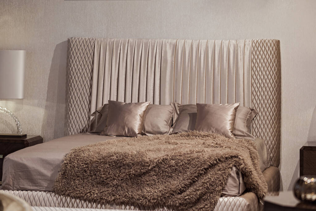 Modische moderne beige Schlafzimmer, Bett, Nachttisch und Lampe, schöne Textilien auf dem Bett. Schickes Schlafzimmerdesign. - Foto, Bild