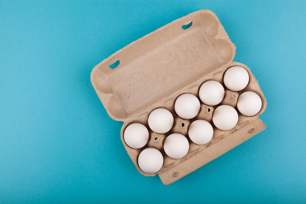 Hühnereier. Draufsicht auf eine offene graue Schachtel mit weißen Eiern. isoliert auf blauem Hintergrund. das Konzept eines gesunden Lebensstils, bei dem man reines Protein bekommt. Richtiges Frühstück. - Foto, Bild