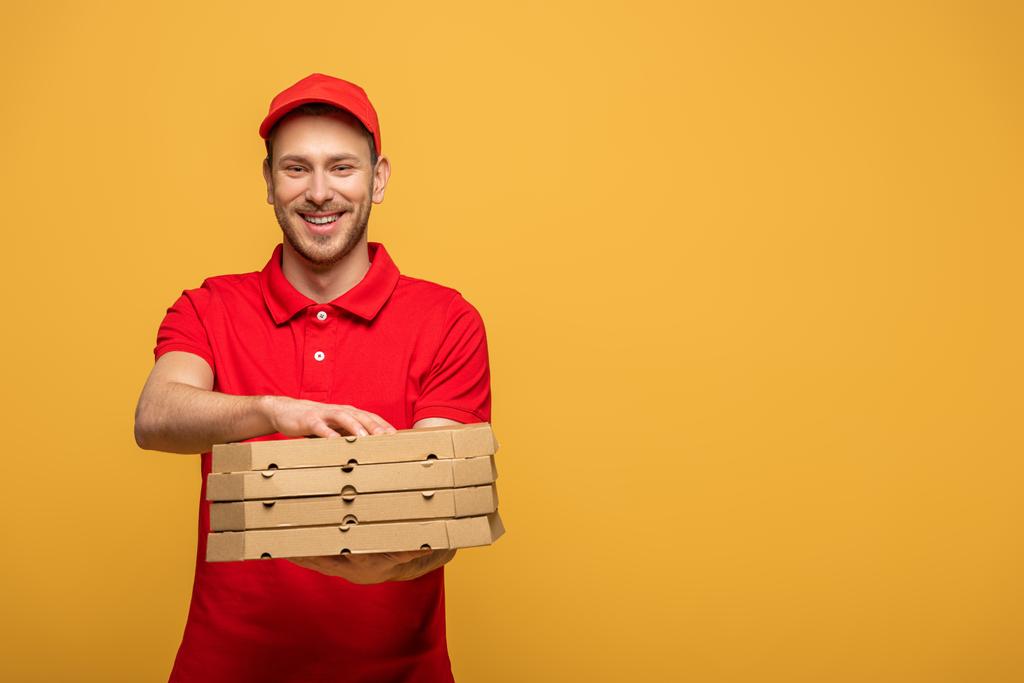 homem de entrega feliz em uniforme vermelho dando caixas de pizza isoladas no amarelo
 - Foto, Imagem