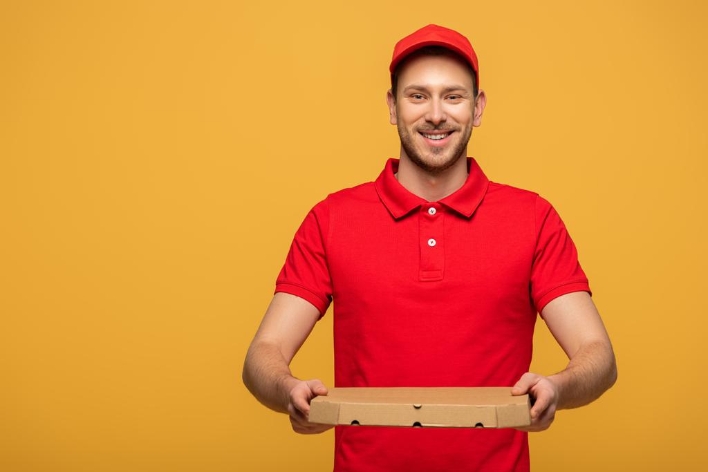 hombre de entrega feliz en uniforme rojo sosteniendo caja de pizza aislado en amarillo
 - Foto, imagen