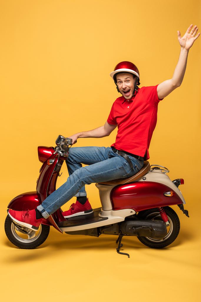 zijaanzicht van de levering man op scooter zwaaiende hand op gele achtergrond - Foto, afbeelding