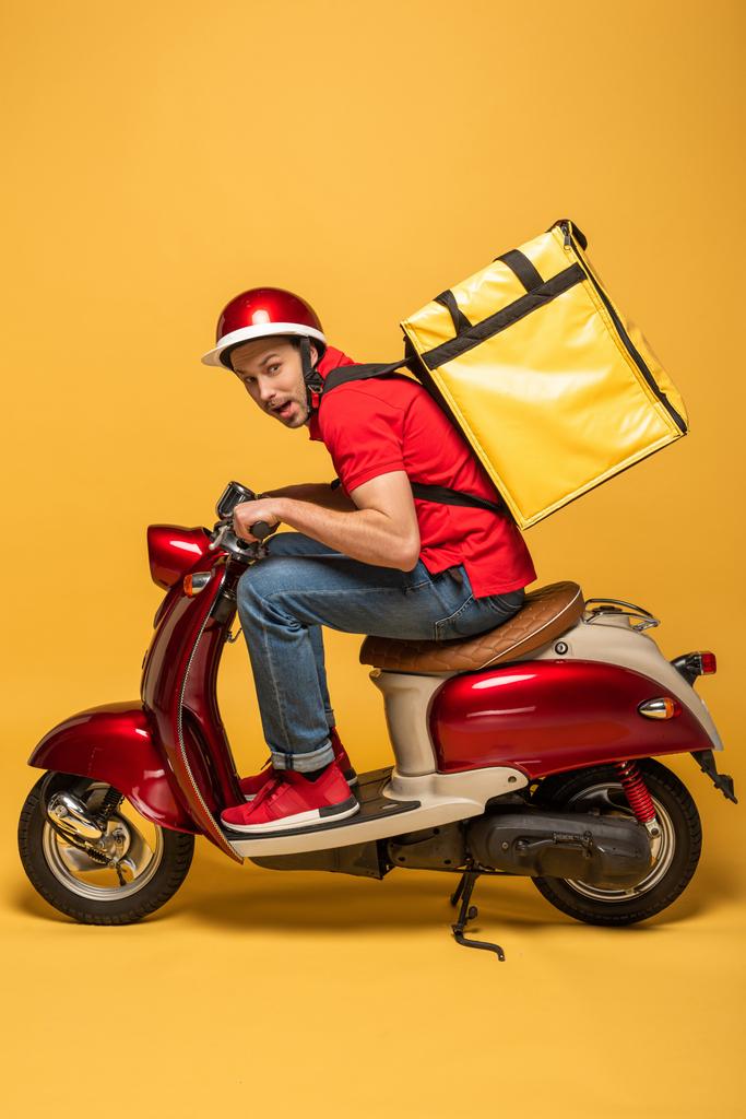 zijaanzicht van de levering man met rugzak op scooter op gele achtergrond - Foto, afbeelding