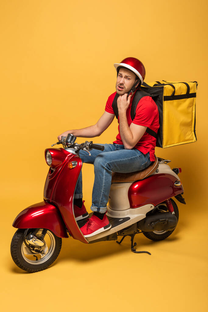 pensive delivery man with backpack on scooter on yellow background - Photo, Image
