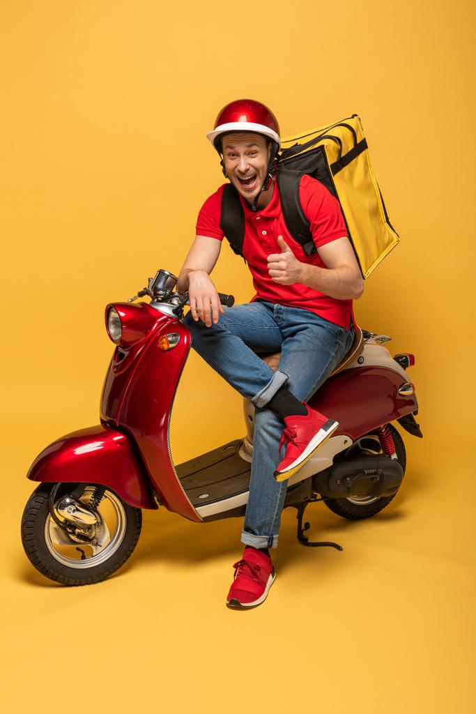 happy delivery man with backpack on scooter showing thumb up on yellow background - Photo, Image
