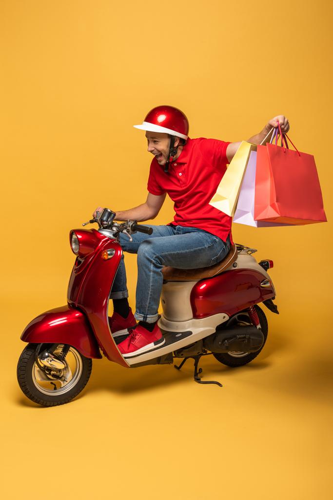 onnellinen toimitus mies punainen univormu ostoskassit skootteri keltaisella taustalla
 - Valokuva, kuva