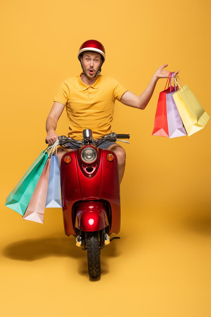 hombre de entrega sorprendido en scooter uniforme amarillo con bolsas de compras sobre fondo amarillo
 - Foto, Imagen