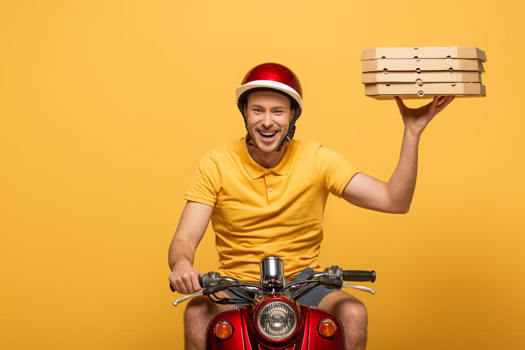 livreur souriant en uniforme jaune scooter équitation avec boîtes à pizza isolées sur jaune
 - Photo, image