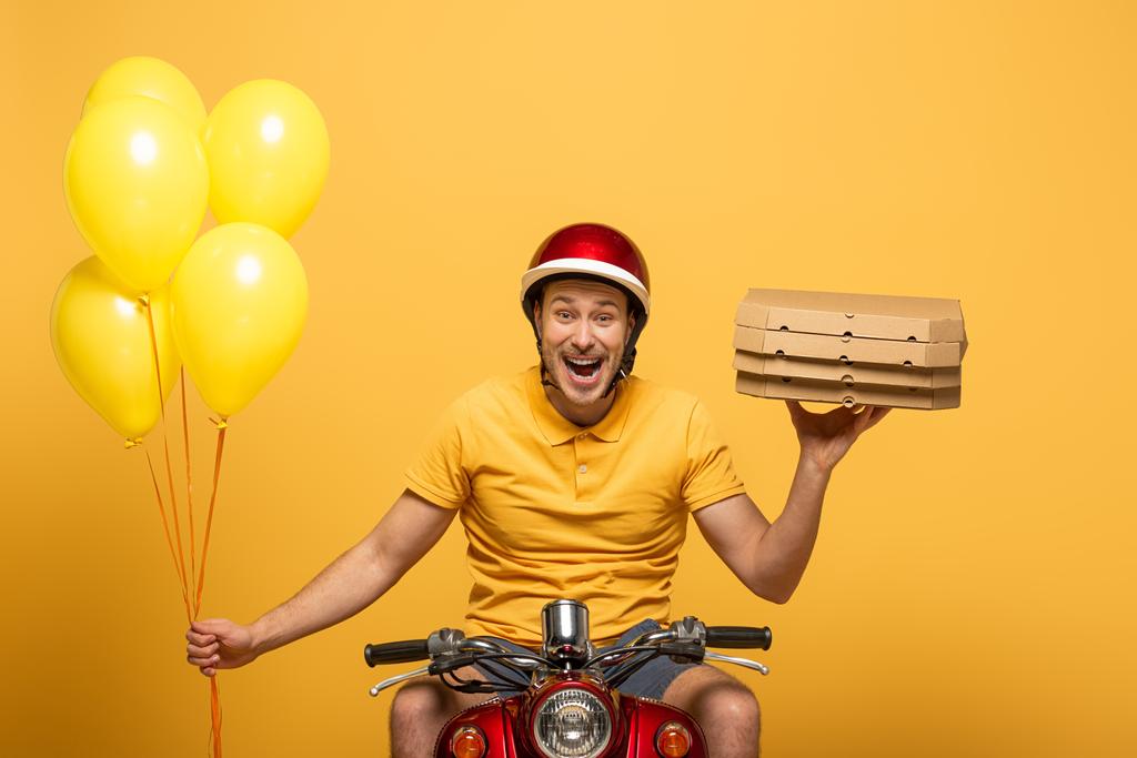 happy delivery man in yellow uniform riding scooter with pizza boxes and balloons isolated on yellow - Photo, Image