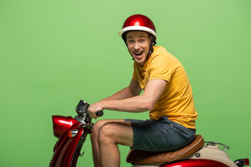 zijaanzicht van gekke levering man in geel uniform op scooter geïsoleerd op groen - Foto, afbeelding