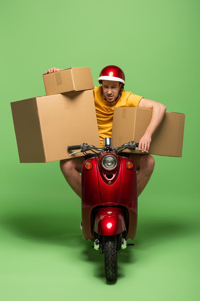 homem de entrega cansado em uniforme amarelo em scooter com caixas em verde
 - Foto, Imagem