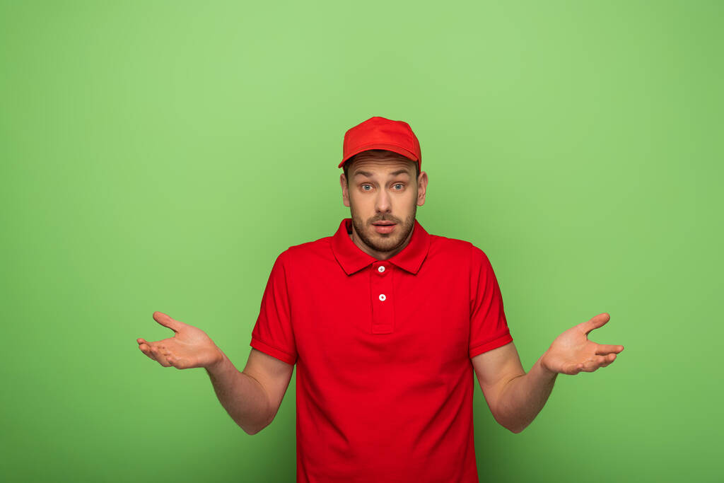confuso uomo di consegna in uniforme rossa che mostra il dubio sul verde
 - Foto, immagini